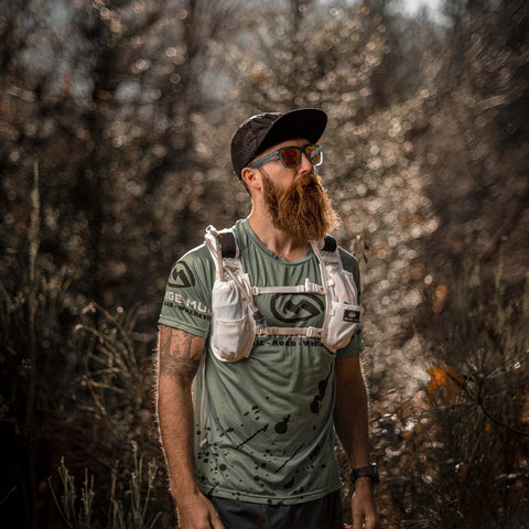 Bearded trail runner in a forest wearing a white Orange Mud hydration vest with soft flasks in the front pockets