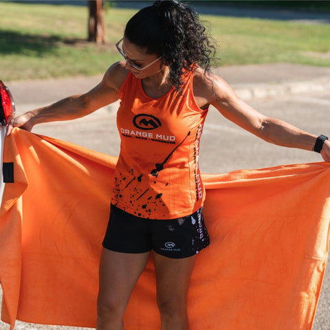 Woman holding an orange Orange Mud Transition Wrap changing towel by her car