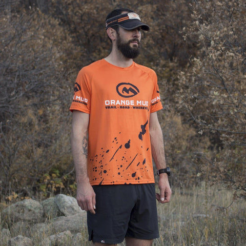 Runner wearing an orange Orange Mud running shirt on a trail